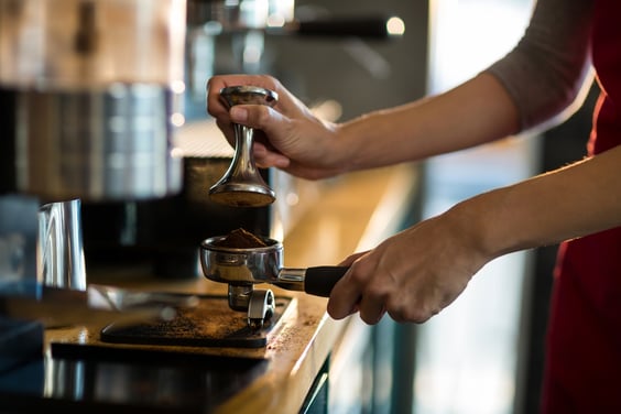 Waiter using a tamper to press ground coffee into a portafilter in cafx92xA9